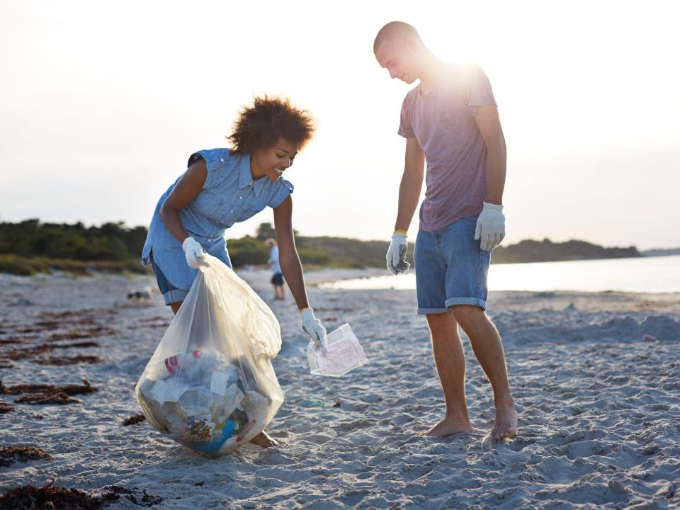 A woman and a man pick up trash from a beach.