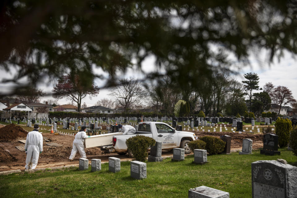 Rabbi Shmuel Plafker, left, watches as a casket is brought for burial at Mount Richmond Cemetery in the Staten Island borough of New York, Wednesday April 8, 2020. Plafker looks at the trees in bloom and the grass sprouting and finds spring's signs of rebirth so paradoxical given the death that surrounds him. He thinks of the centuries-old words he recites on the High Holy Days, that seem to carry so much more weight now. "Who shall perish by water and who by fire? Who by sword and who by wild beast? Who by famine and who by thirst? Who by earthquake and who by plague?" Now, it seems, a plague is upon him. (AP Photo/David Goldman)