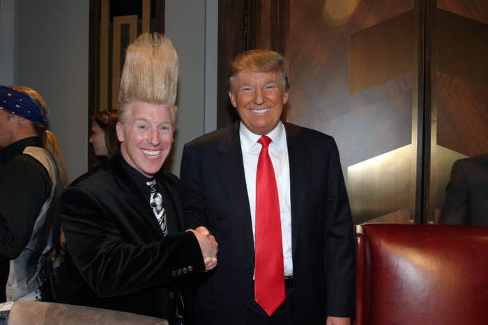 Photo of two men shaking hands. One man, with an exaggeratedly tall mohawk hairstyle, is smiling widely. The other man, Donald Trump, is also smiling and wearing a suit with a red tie