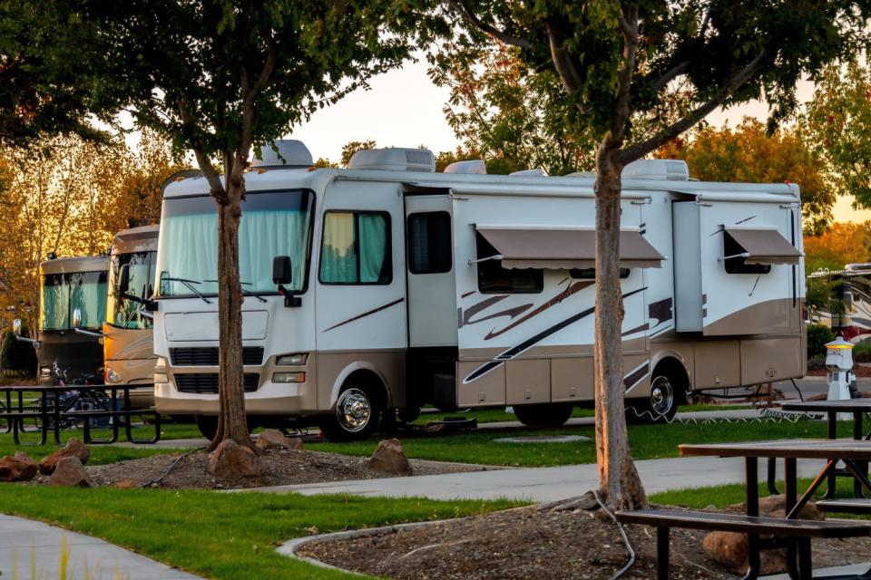 A large RV is parked at a campsite with trees at each lot.