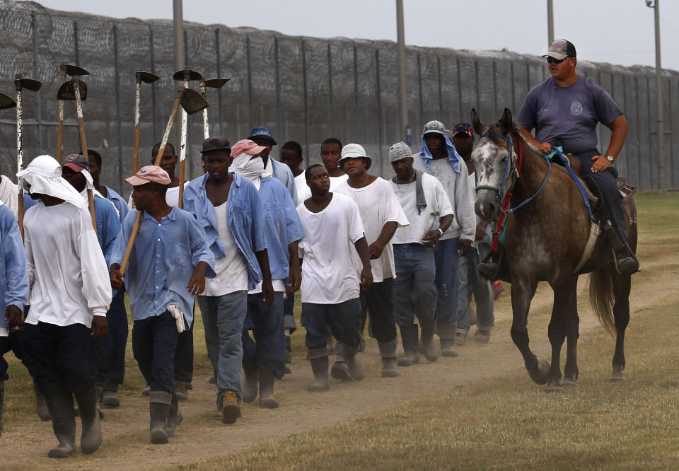 In this Aug. 18, 2011 photo, a prison guard rides a horse alongside prisoners as they return from farm work detail at the Louisiana State Penitentiary in Angola, La. After the Civil War, the 13th Amendment's exception clause, that allows for prison labor, provided legal cover to round up thousands of mostly young Black men. They then were leased out by states to plantations like Angola and some of the country's biggest privately owned companies, including coal mines and railroads. (AP Photo/Gerald Herbert)