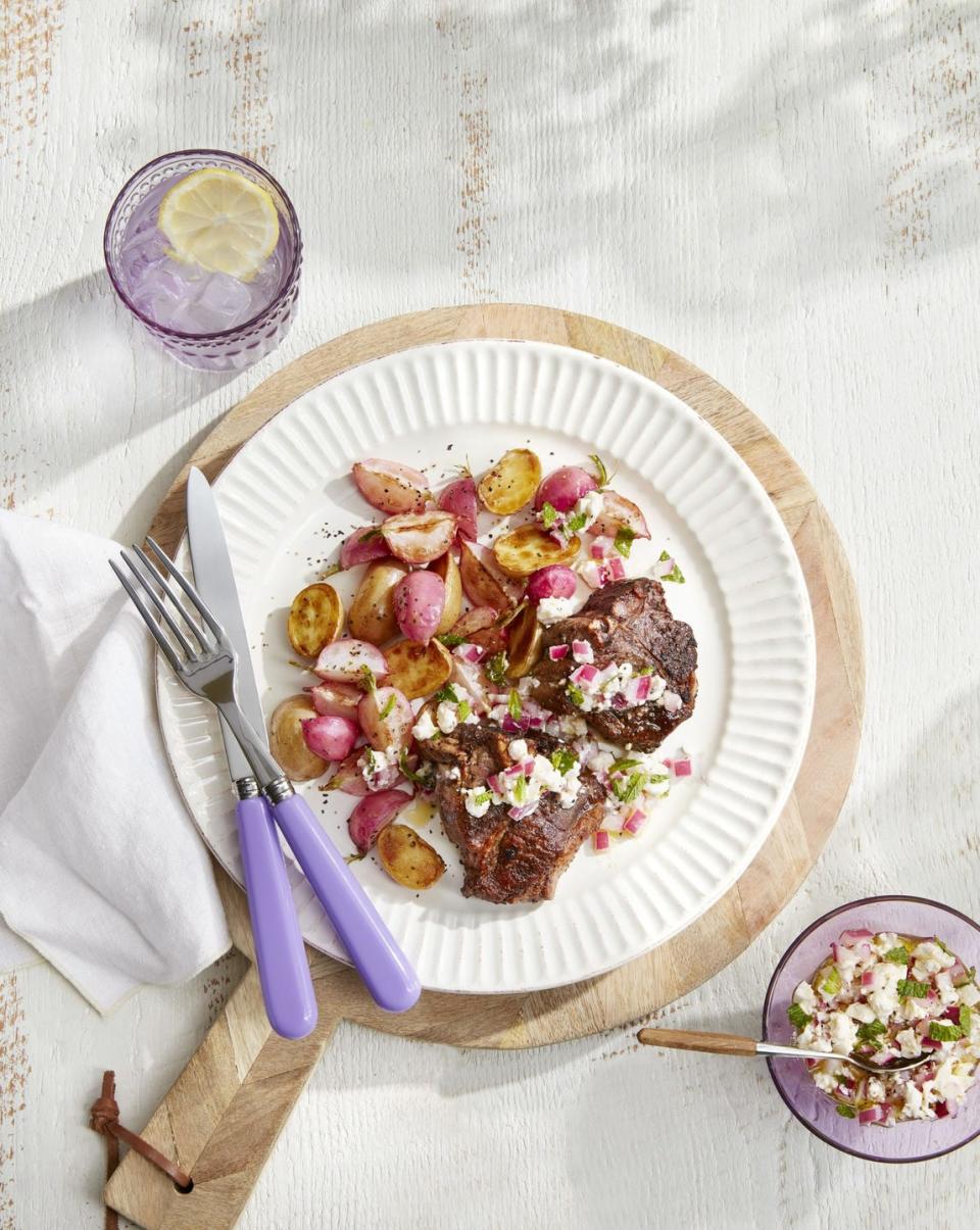 lamb chops with roasted potatoes and radishes on a white plate with silverware and a small bowl of relish on the side