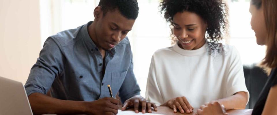 Happy young banking worker watching african ethnicity male client signing mortgage application