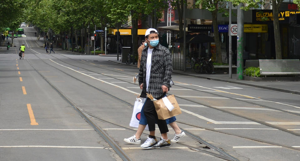 Two people in Melbourne walk along the street with face masks on.