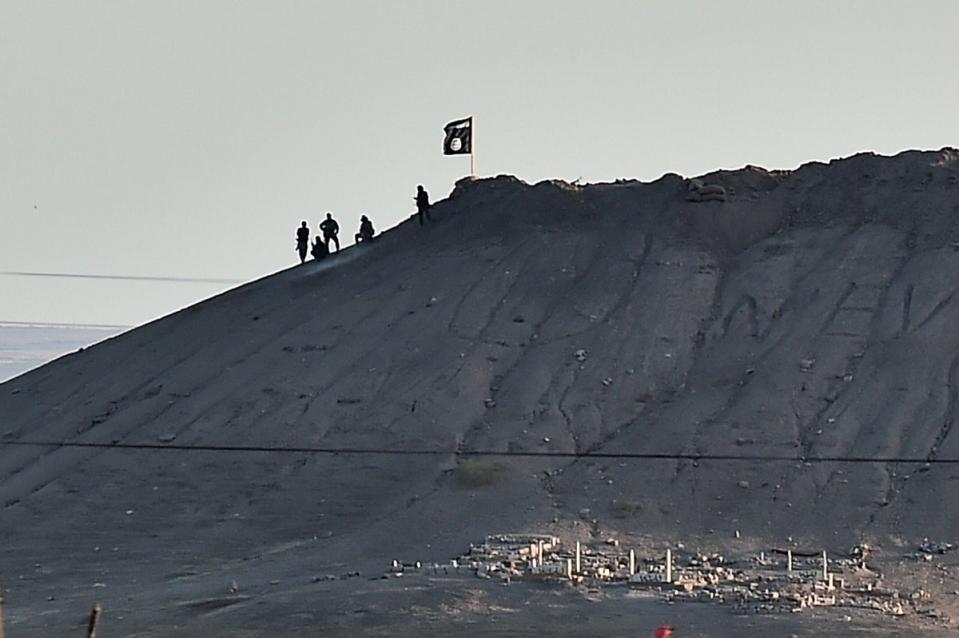 Isis militants sit atop a hill planted with their flag in the Syrian town of Kobani on 6 October 2014. They had been advancing on Kobani since mid-September and by now was in control of the city’s entrance and exit points (AFP/Getty)