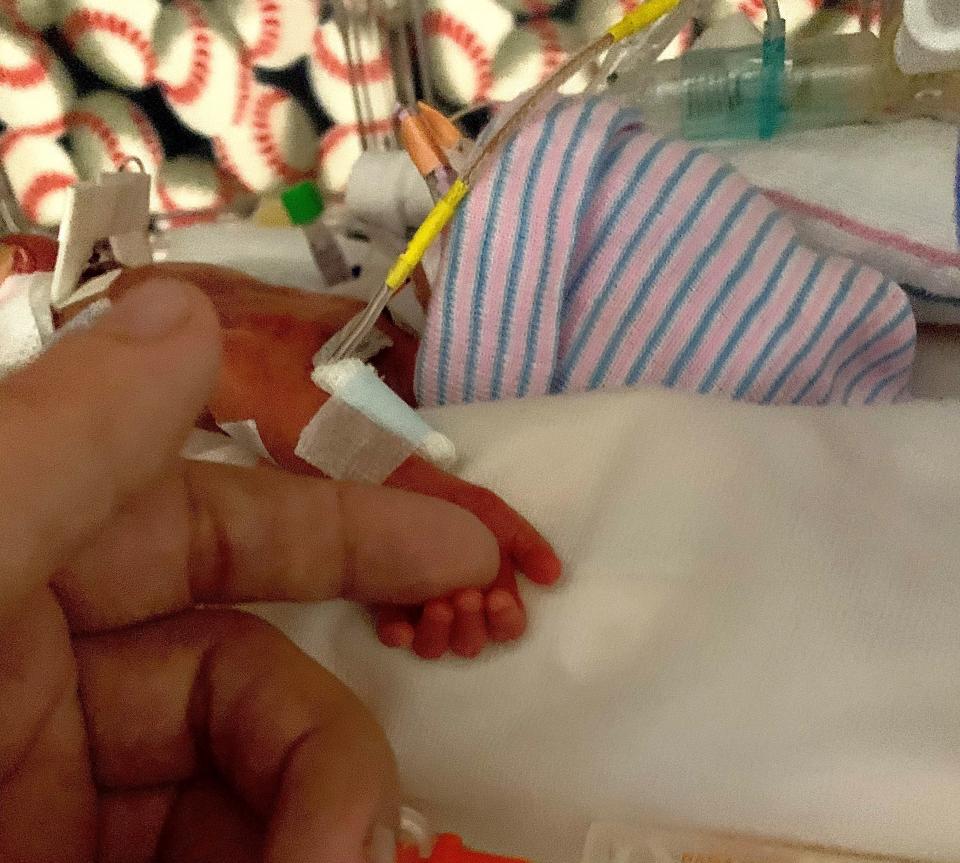 Angela Granger, 41, holds her newborn baby's hand in the hospital. He was born at 27 weeks and spent four months in the NICU.