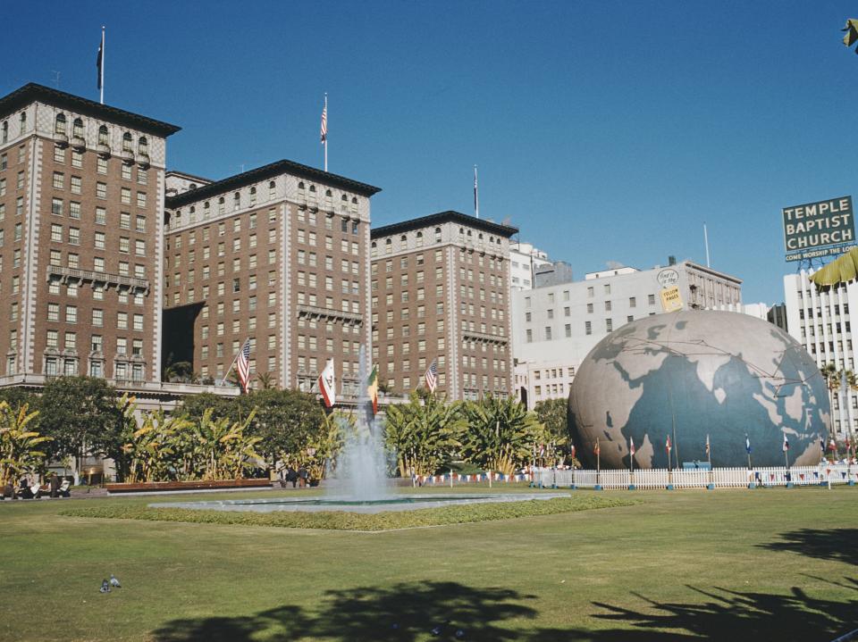 Photo of a green lawn, fountain, large globe statue, and buildings in background.