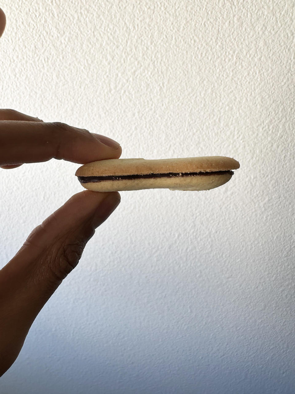 A hand holding a Milano cookie horizontally