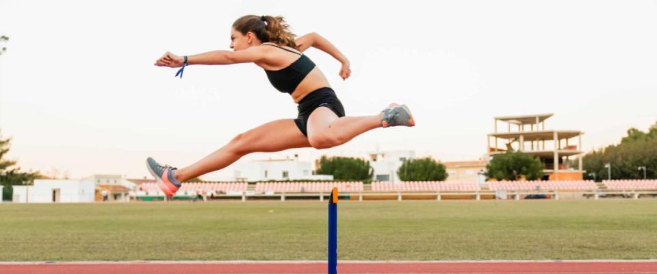 Fit female teenager athlete hurdler running jumping over hurdles