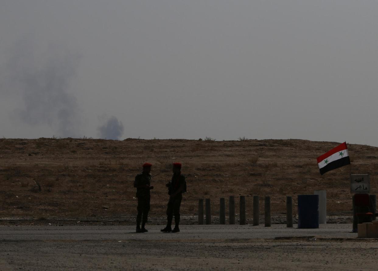 Smoke rises as Syrian army soldiers stand near a checkpoint in Deir Ezzor in this file photo from 21 September, 2017: Reuters