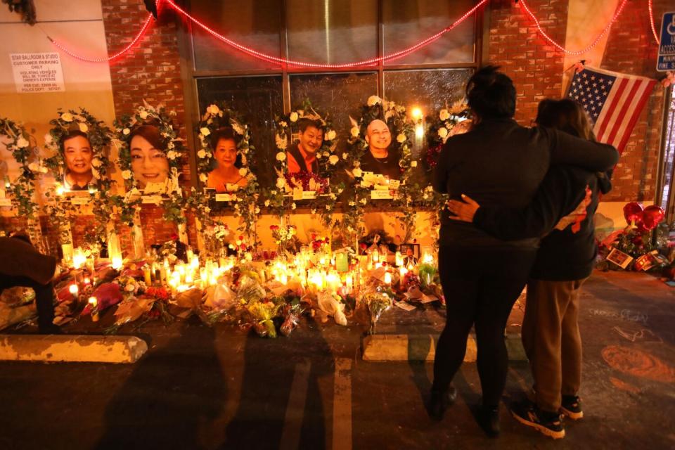 Women comfort each other at a memorial with photos and candles.