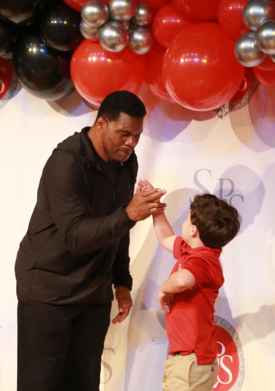 Former University of Georgia running back and current US Senate candidate Herschel Walker gets a high five from a young fan at Savannah Christian Preparatory School.