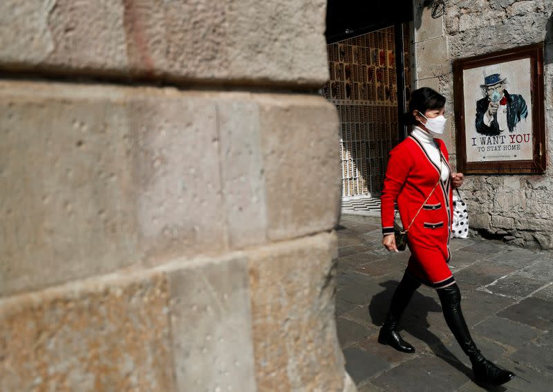 A woman wears a protective mask as she walks past an image of Uncle Sam in a protective mask in Barcelona