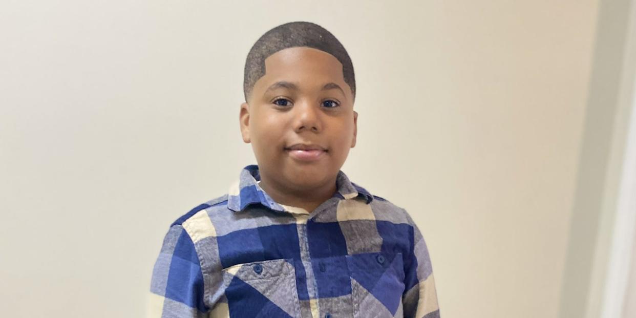 Aderrien Murry standing in front of a white wall while wearing a navy blue and white plaid shirt.