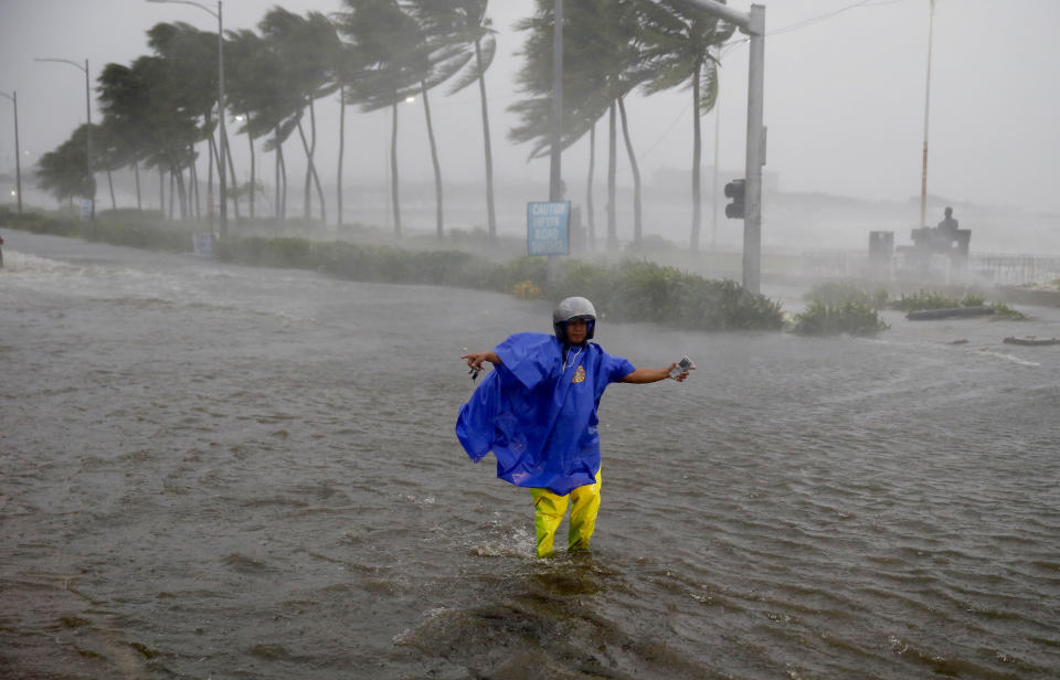 FILE - In this Saturday, Sept. 15, 2018, file photo, a man directs traffic to avoid a flooded street at the onslaught of Typhoon Mangkhut which barreled into the northeastern Philippines before dawn in Manila, Philippines. (AP Photo/Bullit Marquez, File)