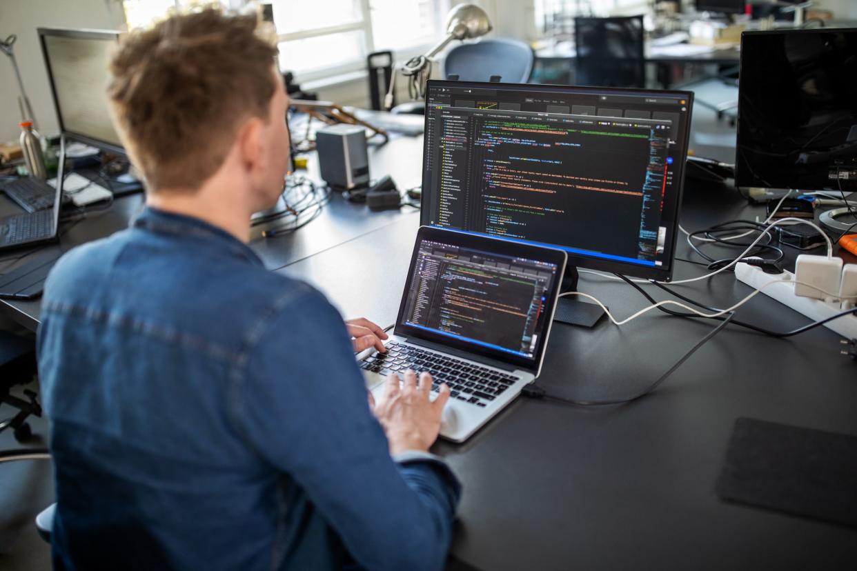 Businessman working on laptop and looking at desktop computer monitor. Male professional sitting at his office desk and working on new software program.