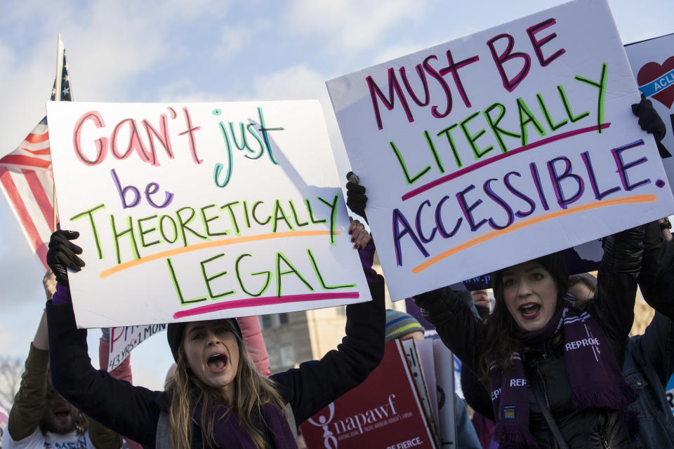 Demonstrators hold signs reading "can't just be theoretically legal" and "must be literally accessible"