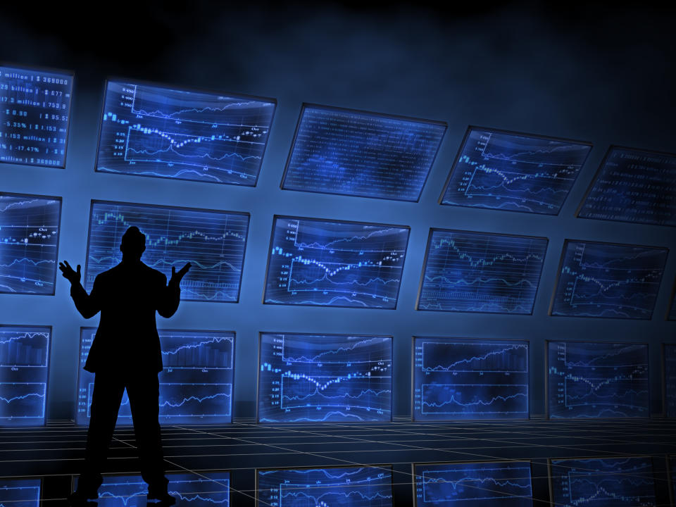 Silhouette of person standing in front of multiple screens displaying charts