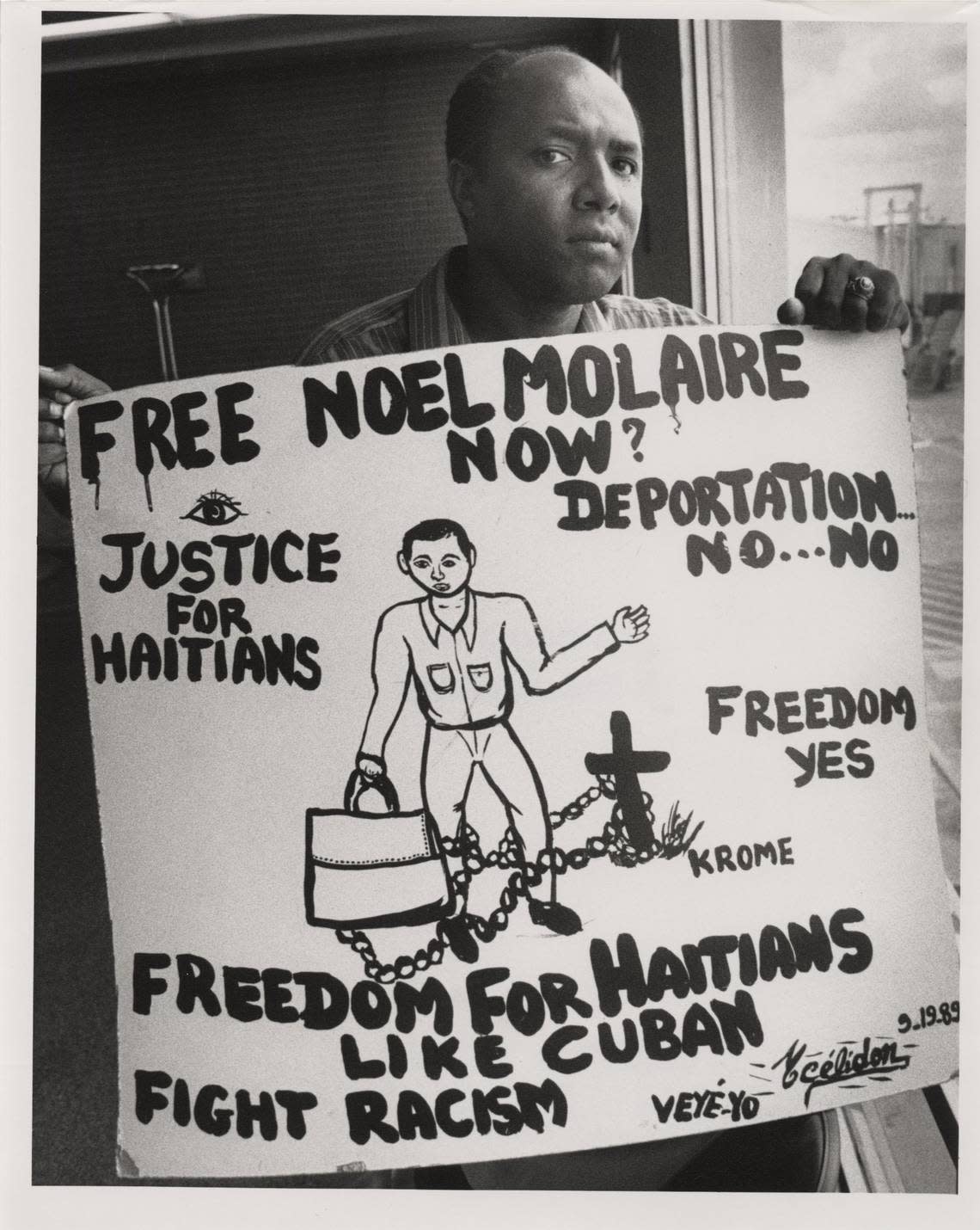 In 1989, The Rev. Gerard Jean-Juste holds a sign protesting the planned deportation of Noel Molaire who fought off another day of being forced back to Haiti. Two other Haitians who were supposed to be taken back also would not get out of the truck the Immigration and Naturalization Service parked out on the tarmac to keep out of view of journalists