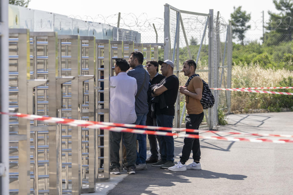 A group of men wait at the turnstiles and speak with survivors, mostly from Pakistan, of a deadly migrant boat sinking at a migrant camp in Malakasa north of Athens, on Monday, June 19, 2023. Hundreds of migrants are believed to be missing after a fishing trawler sank off southern Greece last week. (AP Photo/Petros Giannakouris)