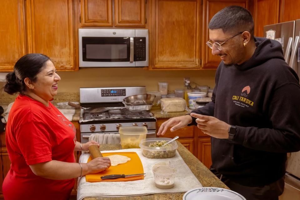 Kulwant "Kimi" Sanghu, left, rolls out the dough for samosas while her son Manu fills the folded dough in their kitchen.