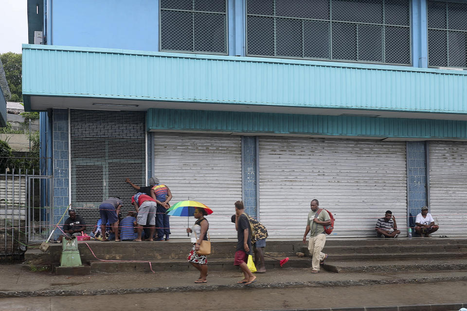 Locals gather outside closed shops in Honiara, Solomon Islands, Monday, Dec. 6, 2021. Lawmakers in the Solomon Islands are debating whether they still have confidence in the prime minister, after rioters last month set fire to buildings and looted stores in the capital.(Gary Ramage via AP)