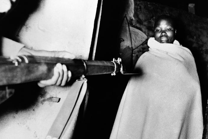 A member of the Mau Mau, wrapped in the blanket in which he was sleeping, is held at gun point during a roundup at 2:30 a.m., by the Fifth Battalion King's African Rifles in the Nyeri district of Kenya on Nov. 13, 1952. Several prisoners were taken, including teachers at the Jomo Kenyatta sponsored Mungari School, where they are accused of spreading Mau Mau doctrines to the pupils. The man in this picture was arrested for being in the possession of subversive literature. (AP Photo, File)