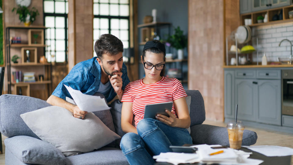 retirement  Couple calculating bills at home using laptop and calculator. Young couple working on computer while calculating finances sitting on couch. Young  man with  wife at home analyzing their finance with documents.