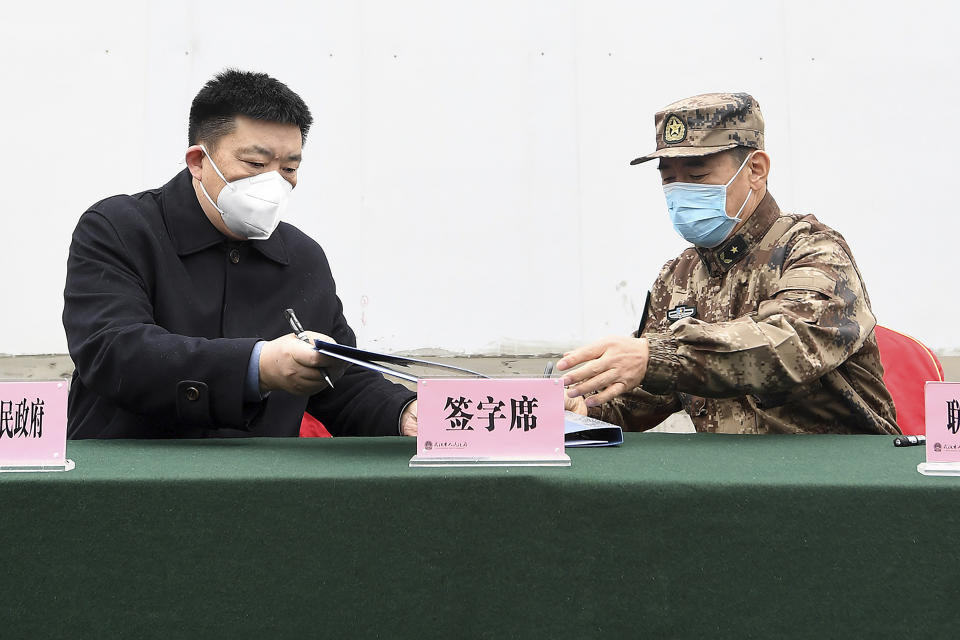 Zhou Xianwang, left, the mayor of Wuhan, exchanges documents with Bai Zhongbin, right, deputy commander-in-chief of China's People's Liberation Army (PLA) Joint Logistic Support Force, during a handover ceremony at the Huoshenshan temporary field hospital in Wuhan in central China's Hubei Province, Sunday, Feb. 2, 2020. The Philippines on Sunday reported the first death from a new virus outside of China, where authorities delayed the opening of schools in the worst-hit province and tightened quarantine measures in a city that allow only one family member to venture out to buy supplies. (Chinatopix via AP)