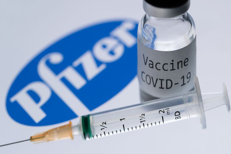 This illustration picture taken in Paris on November 23, 2020 shows a syringe and a bottle reading "Covid-19 Vaccine" next to the Pfizer company logo. (Photo by JOEL SAGET / AFP)