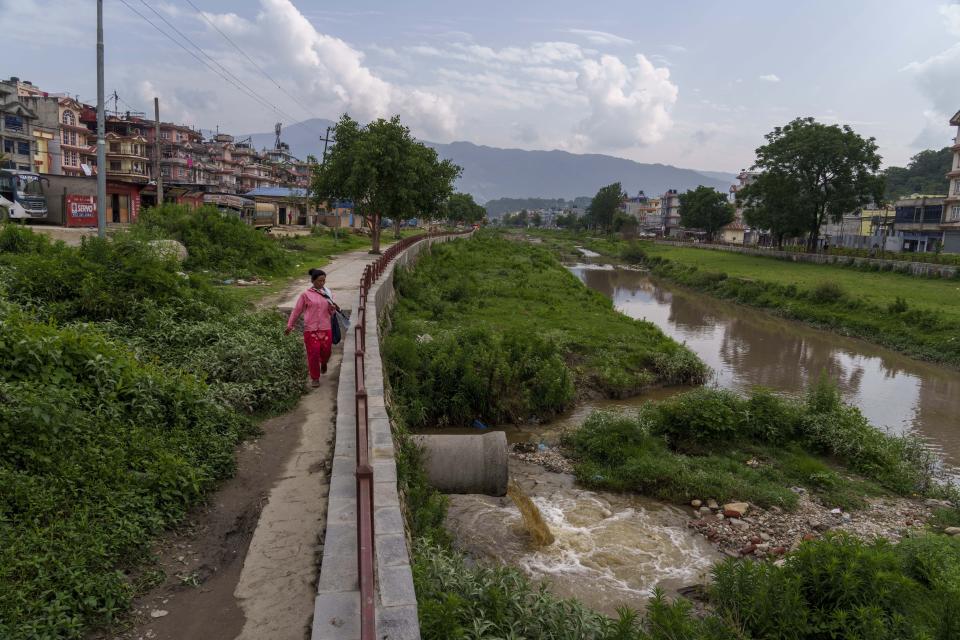 Una mujer pasa junto a tuberías que desaguan en el río Bagmati, en Katmandú, Nepal, el martes 24 de mayo de 2022. (AP Foto/Niranjan Shrestha)