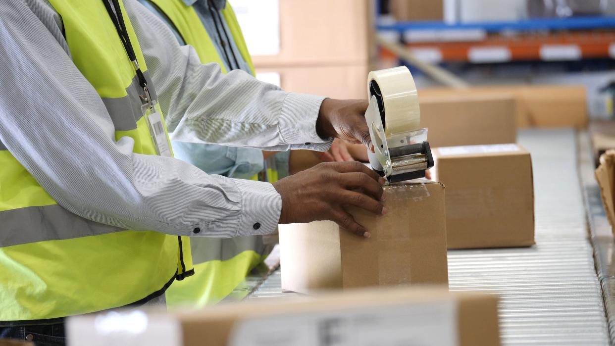 Unrecognizable distribution warehouse workers use tape dispenser to seal a package. They are preparing the package for distribution.