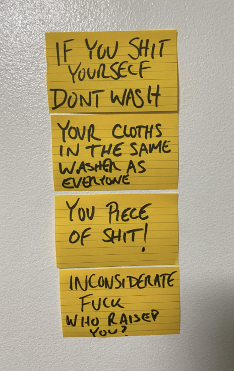 Sticky notes on a wall with handwritten text: "IF YOU SHIT YOURSELF DON'T WASH YOUR CLOTHS IN THE SAME WASHER AS EVERYONE YOU PIECE OF SHIT! INCONSIDERATE FUCK WHO RAISED YOU?"