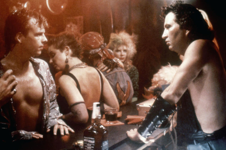 The image shows characters from the film "The Terminator" in a bar scene, including Arnold Schwarzenegger (right) in leather attire, Michael Biehn (left), and various bar patrons in 1980s fashion