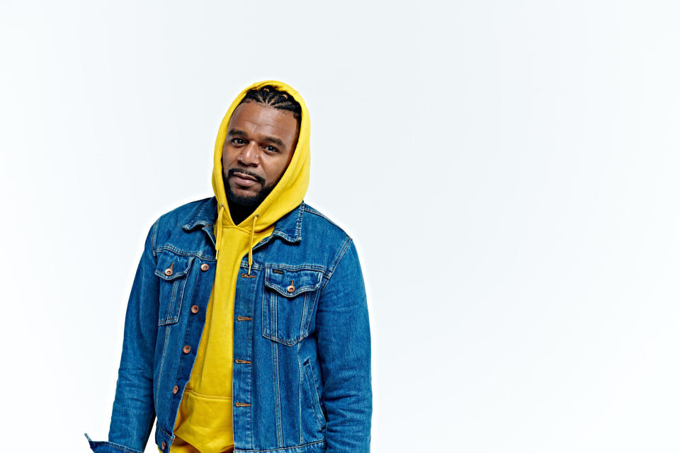 A man in a yellow hoodie looks at the camera