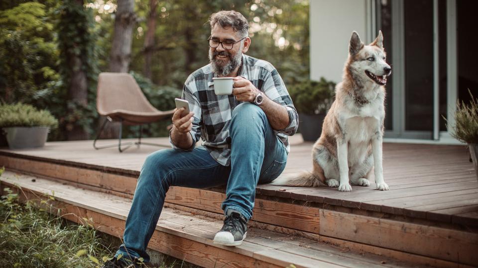 Mature men at his cottage resting on pprch with his dog.