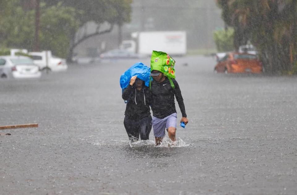 Denis Mendez, 32, left, and Isain Lopez 33, walk down a flooded street in the Edgewood neighborhood on Thursday, April 13, 2023, in Fort Lauderdale, Fla. A torrential downpour severely flooded streets partially submerging houses and cars across South Florida.