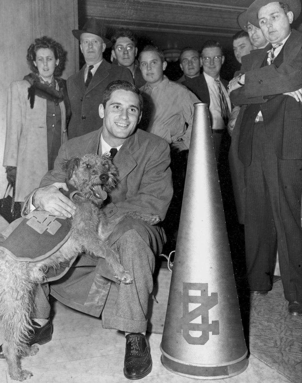 FILE - Notre Dame quarterback Johnny Lujack sits on a suitcase in a hotel lobby holding Notre Dame mascot Clashmore Mike 11, in Cleveland, Ohio, Oct. 31, 1947, after arriving for the Nov. 1 game with Navy. Lujack, the Heisman Trophy winner who led Notre Dame to three national championships in the 1940s, died in Florida on Tuesday, July 25, 2023, following a brief illness. He was 98.(AP Photo/Ed Maloney, File)