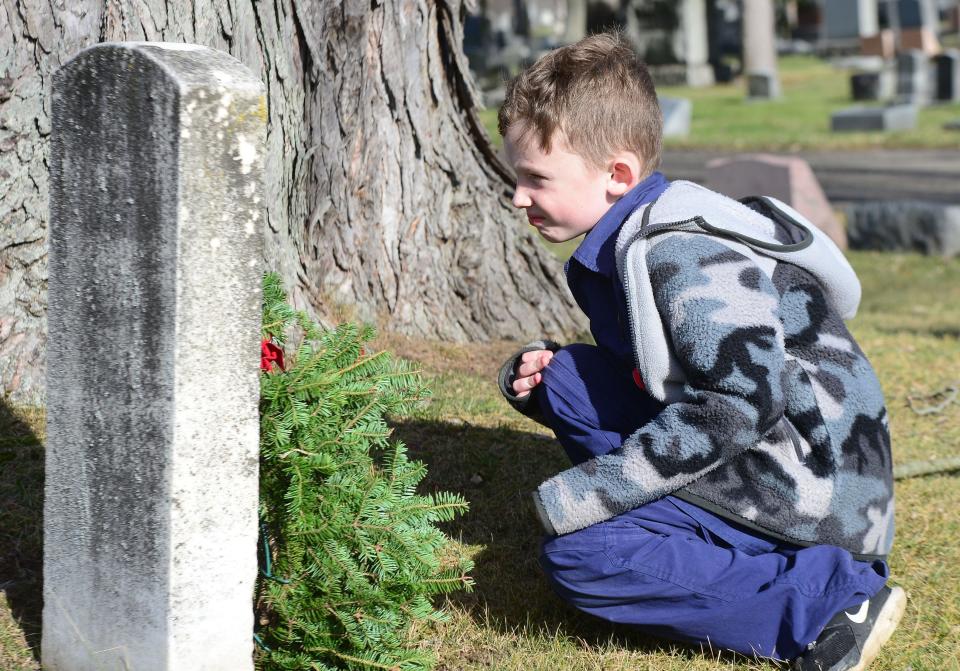 Boston Fleischer, 7, of Boy Scout Troop #2052 reads a veteran's name after placing a wreath on the grave Saturday, Dec. 16, 2023, at Alliance City Cemetery during the Wreaths Across America ceremony.