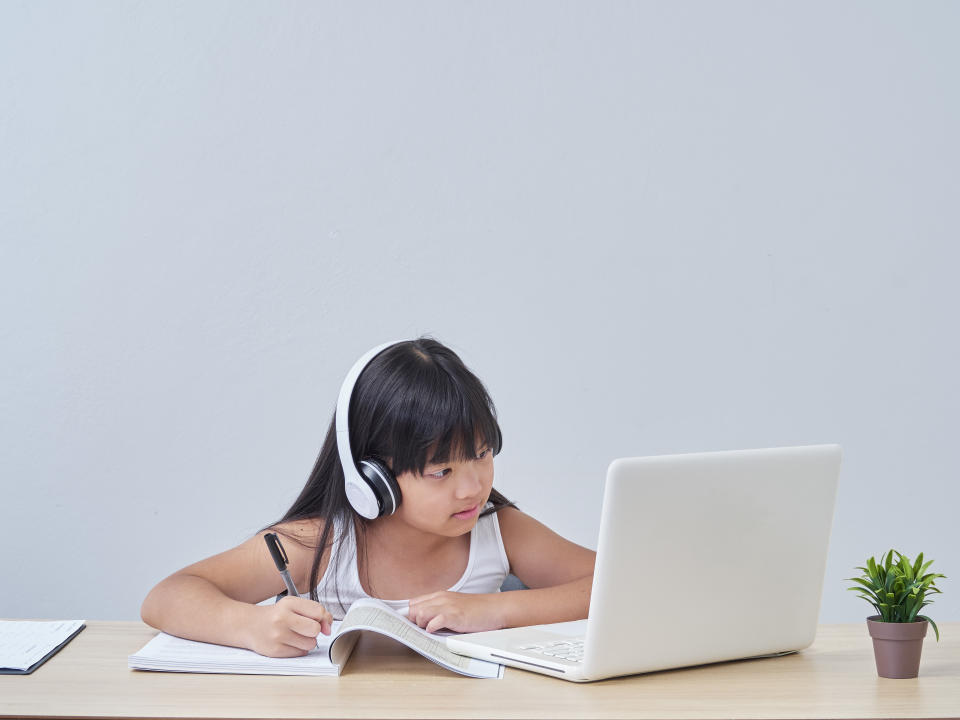 Little girl in headphones and doing online class with laptop at home.