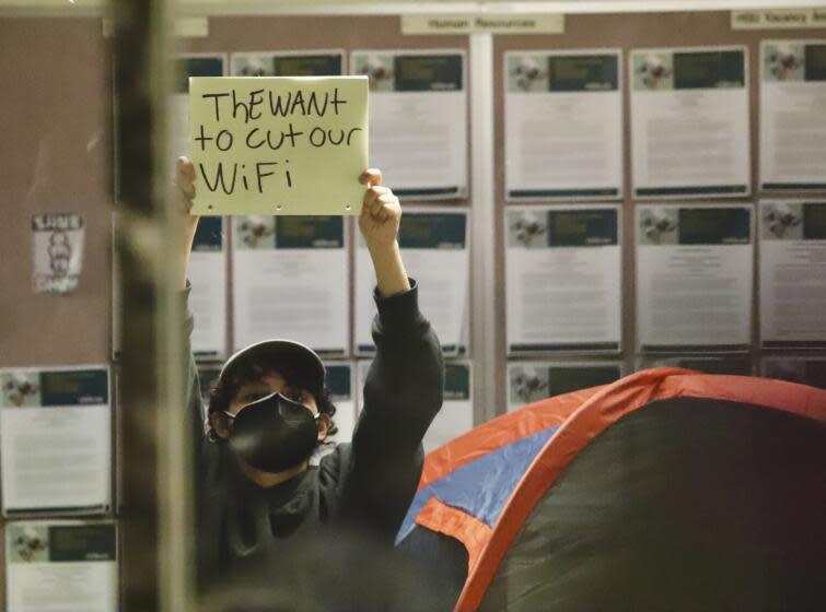 Pro-Palestinian protesters hold up signs while occupying a building on the campus of California State Polytechnic University, Humboldt, in Arcata, Calif., Monday, April 22, 2024. Students at the university used furniture, tents, chains and zip ties to block entrances to an academic and administrative building on Monday. University officials closed the campus through Wednesday. (Andrew Goff/Lost Coast Outpost via AP)