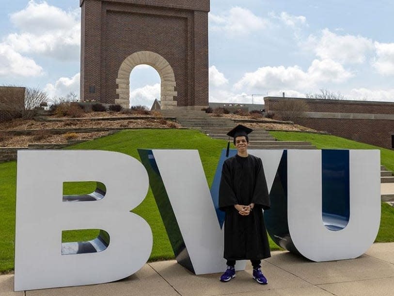 Javier Sarmiento in a cap and gown standing in front of a BVU sign