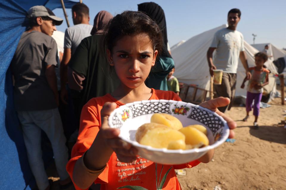 A displaced Palestinian girl shows a bowl of potatos at a refugee camp in Gaza (AFP via Getty Images)