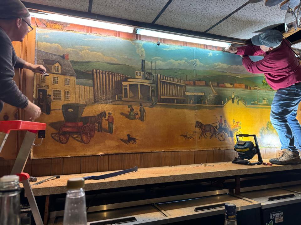 Warren Jones and Dave Cooper work the remove the historic mural, displayed for years behind the bar at the now-closed Magoni's Ferry Landing. The mural has been donated to the Somerset Historical Society.