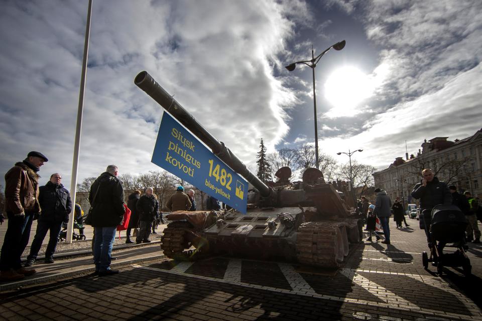People stand by a destroyed Russian tank T-72B decorated with a banner reading "Send money to fight" at Cathedral Square in Vilnius, Lithuania, on March 1, 2023.
