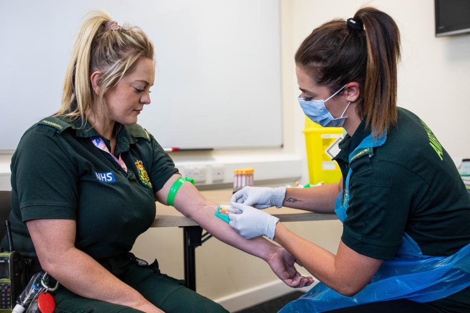 Jess Baddams, a paramedic, right, takes a blood sample from Emily Humpriss, a front line ambulance worker, left, during an antibody testing program at the Hollymore Ambulance Hub, in Birmingham, England, on Friday, June 5, 2020. Making antibody tests widely available may help Britain lift its lockdown restrictions, because they show who has already had the COVID-19 and might have a degree of immunity from coronavirus. (Simon Dawson/Pool via AP)