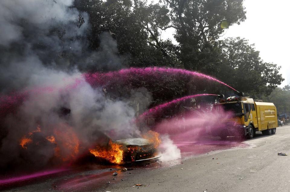 A police vehicle uses colored water to put out flames of a burning vehicle during clashes between police and Jamaat-e-Islami party activists in Dhaka