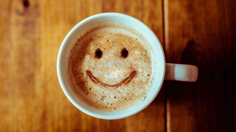 A happy looking Coffee Cup on a brown rustic table.