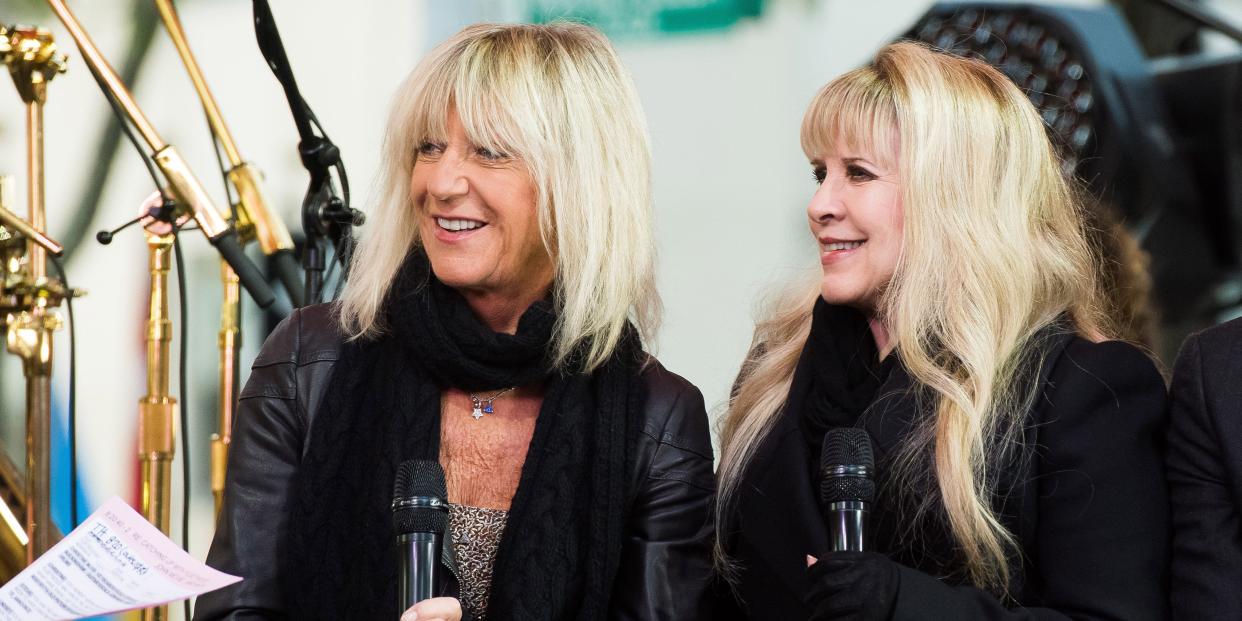 Christine McVie and Stevie Nicks sit next to each other on a stage.