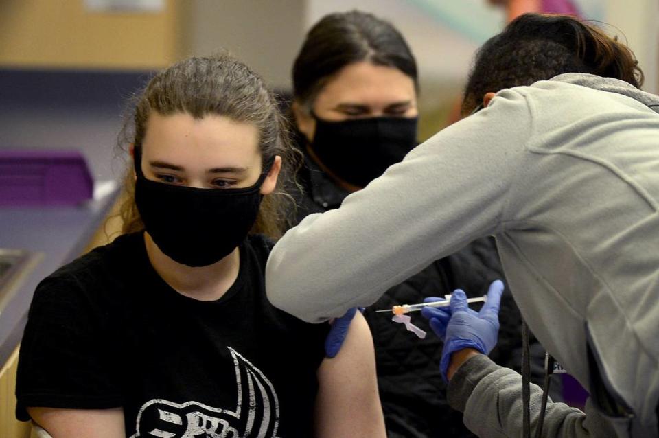 Elise Arnold, 15 years, left, receives her first COVID vaccination shot on Wednesday, May 12, 2021 at the Novant Health clinic at 6070 East Independence Blvd. Looking on in the background is EliseÕs mother, Charity Arnold.